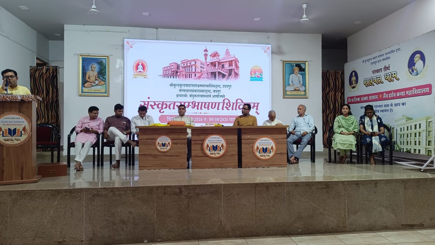 The guests of the inauguration seated in a row on the dais before the projected camp announcement